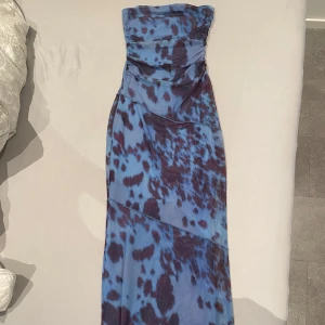 Blå mönstrad långklänning Bershka - Säljer en snygg axelbandslös långklänning från Bershka i blått med mörka fläckiga mönster. Klänningen har en figurnära passform och är tillverkad i ett stretchigt syntetmaterial. 