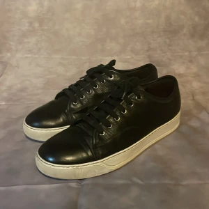 Svarta Lanvins - Stilrena svarta sneakers från Lanvin i äkta skinn med vit platt sula. Klassisk design med rund tå, svarta skosnören och diskreta metalldetaljer vid snörningen. Nypris runt 4500, mitt pris 1099. 7,5/10 skick. Pris kan diskuteras vid snabb affär. Uk Size 7 så storlek 41-42