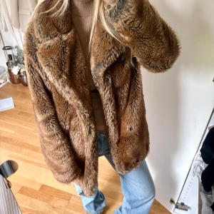 Brun pälsjacka med oversized passform - Säljer en fluffig och snygg brun pälsjacka med bred krage och lång ärm. Jackan har en oversized vibe och är perfekt för dig som vill sticka ut. Fodrad insida och mjukt material som känns lyxigt. Passar dig som gillar statement-plagg och vill hålla dig varm.