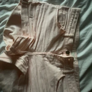 Ljusrosa jeansshorts från H&M - Säljer ett par ljusrosa jeansshorts från H&M med klassisk femficksdesign och låg/medel midja. Shortsen har dragkedja och knapp framtill, samt bälteshällor. Perfekta för varma dagar och ger en fräsch vibe till din outfit.