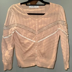 Ljusrosa kofta med spets från Designers Remix - Supersöt ljusrosa kofta från Designers Remix med spetsdetaljer och knappar framtill. Ärmarna är något kortare. Någon söm som släppt lite, men inget man tänker på (se bild).