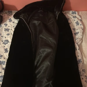 Svart pälsjacka med bälte från MISU - Snygg svart pälsjacka från MISU Studio Collection i storlek 36. Jackan har ett mjukt pälsmaterial, dragkedja framtill och ett brett bälte i midjan för extra stilpoäng. Perfekt för dig som vill ha en statementjacka med lyxig känsla.