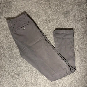 Grå chinos från Mason's, stl 48 - Snygga grå chinos från Mason's i storlek 48. Byxorna har klassisk passform med raka ben, bakficka med knapp och diskreta detaljer. Tillverkade i en mjuk bomullsblandning med lyocell och elastan för extra komfort. Clean.