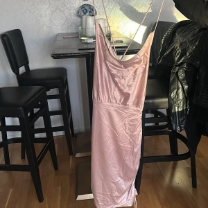 Champagnefärgad långklänning Bubbleroom - Säljer en elegant långklänning från Bubbleroom i champagnefärgad satin. Klänningen har tunna axelband som korsas i ryggen, draperad urringning och snygg knytning bak. Materialet är glansigt och ger en lyxig känsla. Perfekt för dig som vill sticka ut.