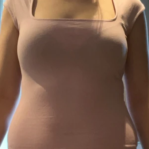 Ljusrosa topp med fyrkantig ringning - Säljer en ljusrosa topp med snygg fyrkantig ringning och korta ärmar. Toppen är figurnära och har en enkel, stilren design som passar perfekt till jeans eller kjol. Tillverkad i mjukt bomullsmaterial för en bekväm känsla hela dagen.