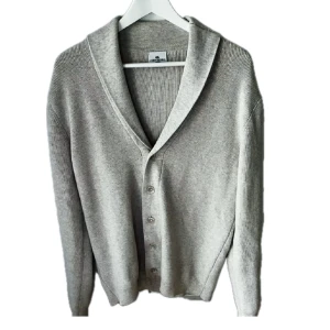 Ljusgrå kofta från John Henric - Snygg ljusgrå kofta från John Henric med ribbad struktur och klassisk sjalkrage. Koftan har knappar framtill och är långärmad, perfekt för lager-på-lager. Tillverkad i mjuk bomull som känns skön mot huden och passar till många olika stilar.