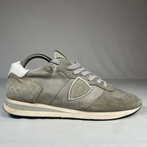 Grå/gröna Philippe Model sneakers mocka/läder - Snygga sneakers från Philippe Model i en ljusgrå färg med detaljer i mocka och läder. Skorna har klassisk snörning, rund tå och vit sula med grå rand. Ikonisk sköld-logga på sidan och mjuk vadderad plös med märkning. Perfekta för en stilren och avslappnad look. Storlek 42. Mitt pris 1099kr! Hör av er vid frågor!