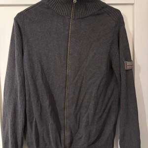 Grå ribbad kofta med dragkedja - Säljer en grå ribbad kofta från Northbrook med hel dragkedja framtill och hög krage. Ärmarna och ryggen är ribbstickade för en snygg struktur. Perfekt för lager-på-lager och chill vardagsstil.