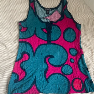 Färgglad linnetopp Marimekko x H&M - Säljer en unik linnetopp från Marimekko x H&M med stort grafiskt mönster i turkos och ceriserosa. Toppen är ärmlös, har rund halsringning och knappar framtill. Materialet är mjuk bomull.