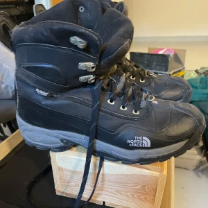 Svarta kängor från The North Face - Svarta kängor från The North Face med HydroSeal-teknologi. Grov sula för bra grepp, snörning med metallhakar och robust design. Perfekta för kalla och blöta dagar. Materialmix av syntet och skinn för extra hållbarhet och komfort.