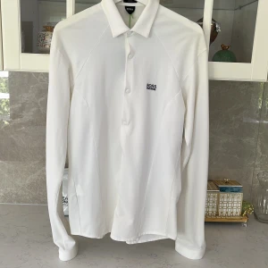 Vit slim fit skjorta från Hugo Boss - Vit långärmad skjorta från Hugo Boss med stretchigt material och slim fit-passform. Skjortan har klassisk krage, knappar framtill och diskret broderad logga på bröstet. Perfekt för dig som gillar stilrena och moderna plagg.