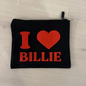 Svart Billie Eilish necessär med röd text! - Cool svart necessär med dragkedja och trycket 'I ❤️ BILLIE' i rött framtill. Perfekt att ha småsaker eller smink i. Enkel och smidig att ta med sig i väskan.