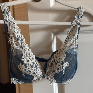 Intimissmi bh - Säljer en snygg blå bralette från intimissmi med vackra broderade spetsdetaljer i vitt. Toppen har breda axelband och transparent mesh med blommönster framtill. Perfekt för att ge outfiten en extra touch av stil.