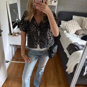 Leopardmönstrad blus med knyt - Säljer en kortärmad blus med leopardmönster och v-ringning. Blusen har knyt framtill och är i en loose passform, perfekt för att ge outfiten edge. Färgerna går i svart och beige med inslag av brunt. Superfin att styla med jeans eller kjol.