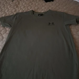 Grön t-shirt från Under Armour - Snygg grön t-shirt från Under Armour med klassisk logga tryckt på bröstet. T-shirten har rund halsringning och korta ärmar, perfekt för en sportig och clean look. Materialet är mjukt och skönt, passar perfekt till träning eller chill.