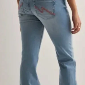 Nelly bootcut jeans - Snygga ljusblå bootcut jeans från Nelly med klassisk femficksdesign och coolt rött broderi på bakfickorna. Jeansen har låg midja och är tillverkade i mjukt bomullstyg med en lätt stretch. Perfekta för en avslappnad och trendig look.