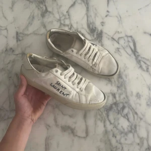 Saint Laurent vita sneakers med snörning - Hejsan! Jag säljer dessa riktigt feta skor ifrån saint Laurent i storlek 39-40. Dem är i helt okej skick inte jätte bra! Sulan sitter lite dåligt som man kanske ser på bilden men den sitter fast ändå och om man hade velat laga de så kan man fixa det med Lim eller vad som helst! Hör av er om ni har några frågor!😊