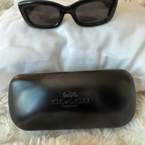 Svarta solglasögon från Coach - Snygga svarta solglasögon från Coach med rektangulära bågar och mörka glas. Kommer med originalfodral i svart med Coach-logga. Perfekta för en stilren look och passar till alla outfits.