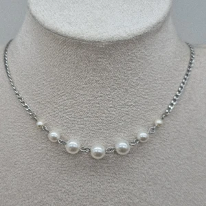 Silverhalsband med pärlor - Stilrent halsband med silverfärgad kedja och sju vita pärlor i olika storlekar framtill. Kedjan har klassisk länkdesign och pärlorna ger en elegant touch. Perfekt accessoar för att lyfta din outfit.