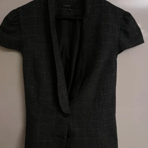 Chik kookai plaid Blazer - Elegant women's blazer by Kookai - Dark plaid pattern with fine white lines, featuring a flattering fitted cut, shawl collar, front buttons, and unique lace-up detail at the hem. Perfect for both casual and chic occasions.