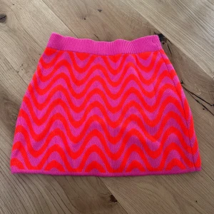 Rosa och röd vågig stickad kortkjol - Superfin stickad kortkjol med vågigt mönster i rosa och rött. Kjolen har en bred ribbad midja i rosa och är perfekt för dig som gillar färgstarka statement-plagg. Materialet är mjukt och stretchigt för en bekväm passform. Har klippt av lapparna, men den är från HM i storleken XS