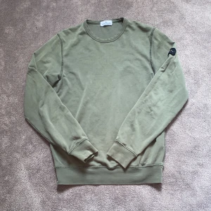 Grön sweatshirt från Stone Island  - Säljer en stilren grå sweatshirt från Stone Island med en klassisk rund hals och ikonisk patch på vänster ärm. Tröjan har långa ärmar och är tillverkad i mjuk bomull, perfekt för en chill och snygg look. Storlek XS/S (170) Vid minsta fundering hör av dig så varar jag direkt! 