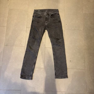 Svarta jeans från J.Lindeberg, 30/32 - Säljer ett par svarta/grå jeans från J.Lindeberg i storlek 30/32. Jeansen har klassisk femficksdesign, raka ben och normal passform. Snyggt diskret JL-logo på myntfickan och stilren tvättad svart färg. Perfekta för dig som gillar en enkel och clean look.