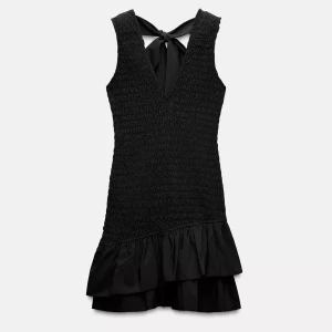 Svart kort klänning med volang - Supersnygg svart klänning med smockad överdel, v-ringning och volangkant nedtill. Klänningen är ärmlös och har en fin knytning i ryggen som ger en extra detalj. Perfekt för dig som gillar stilrena och trendiga plagg. Använd 1 gång Zara 