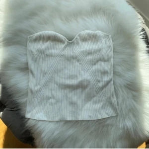 Vit ribbad tubtopp från Lindex - Supersnygg vit korsettopp från Lindex i ribbat material. Toppen är axelbandslös med en hjärtformad byst och markerade sömmar framtill som ger en cool siluett. Perfekt att styla med jeans eller kjol för en trendig look.