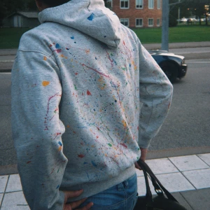 Grå hoodie med färgstänk - Säljer en grå hoodie med coola färgstänk i blått, rött, gult, grönt och orange. Tröjan har huva, känguruficka och långa ärmar. Perfekt för dig som vill sticka ut med en unik streetstyle-look. Storleken är S/M men sitter lite mer som S