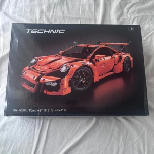 Technic Porsche 911 GT3 RS 42056 - LEGO Technic Porsche 911 GT3 RS, modell 42056, med 2704 delar. Bygg en detaljerad sportbil med autentiska funktioner som fungerande växellåda, ratt, fjädring och detaljerad motor. Förpackningen ser ut att vara i mycket gott skick, perfekt för samlare eller byggentusiaster.