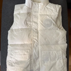 Vit dunväst från Canada Goose - Säljer en snygg vit dunväst från Canada Goose i storlek M/L. 10/10 skick helt oanvänd!. Säljer den efter som att den är för stor. Möts bara upp i Stockholm! 