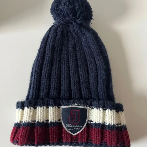 Randig stickad mössa med tofs - Mysig stickad mössa från Jacson i marinblått, vinrött och vitt.