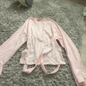 Ljusrosa långärmad topp från Nelly knyt bak - Supersöt ljusrosa långärmad topp från Nelly med knytband i midjan och öppen rygg. Toppen har en croppad passform och är tillverkad i mjuk bomull, perfekt för en trendig look. Enkel men ändå unik detalj med knytet bak.