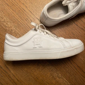 Vita sneakers från Tommy Hilfiger - Snygga vita sneakers från Tommy Hilfiger med diskret logga på sidan och bak på hälen. Skorna har snörning, rund tå och är gjorda i skinn med vit sula. Perfekta för en clean och stilren look.