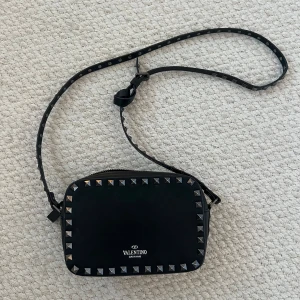 Svart axelväska med nyttar - Säljer en svart axelväska med coola nitar runt kanterna. Väskan har justerbar axelrem och dragkedja upptill. Perfekt för dig som vill ha en edgy och stilren accessoar till din outfit.