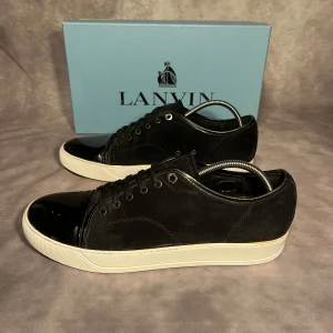Svarta sneakers från Lanvin med lackad tå - Snygga svarta sneakers från Lanvin i storlek uk 10 sitter som eu 44-45. Skorna är i bra skick sulan har blivit solblekt och lite repor se bild mycket liv kvar i dom såklart. Bara skorna fås med, sitter ett par replacment snören på. Sulkräm har använts för att fräscha upp skorna.