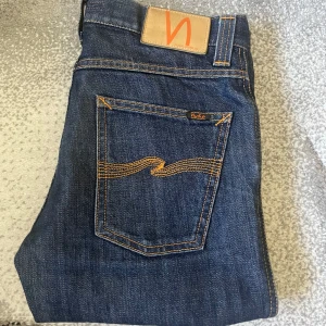 Nudie Jeans, Straight Fit. 29/32 - Feta mörkblå jeans från Nudie Jeans med klassisk orange söm på bakfickorna. Modellen har rak passform och den klassiska femfickors modellen tillverkade i slitstarkt bomullsjeansmaterial. Perfekt för dig ifall du gillar lite washed jeans men ändå perfekt skick. Har inget namn på modellen för de är borttvättat. Jeansen sälj inte längre så du får de för ett riktigt bra pris. Skriv vid intresse eller frågor 🙌