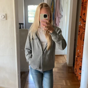 Grå zip-hoodie från Blue - Säljer en grå hoodie från Blue med dragkedja framtill och två fickor. Tröjan har huva.