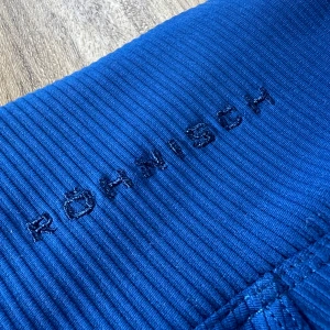 Blå ribbade leggings från Röhnisch XS - Snygga blå leggings från Röhnisch i ribbat material. De har hög midja och en smidig ficka på benet, perfekta för träning eller chill. Materialet är stretchigt och följsamt, och färgen är riktigt klarblå. Loggan är broderad framtill i samma ton.