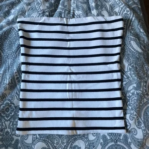 Randig vit och svart tubtopp - Säljer en stilren tubtopp med svarta horisontella ränder på vit botten. Toppen är bandeau-modell och ärmlös, perfekt för sommardagar. Gjord i mjukt bomullsmaterial som sitter skönt mot huden. Enkel att matcha med jeans eller kjol för en avslappnad look.