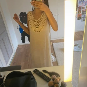 Beige långklänning med virkad detalj - Säljer en beige långklänning med snygga virkade detaljer vid halsringningen och ryggen. Klänningen är ärmlös och har en djup öppen rygg, perfekt för sommardagar. Materialet känns lätt och luftigt, och modellen är rak och avslappnad.