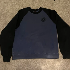 Blå och svart sweatshirt från Spitfire - Sweatshirt från Spitfire Wheels i blått med svarta ärmar och stora tryck på ryggen. Klassisk crewneck-modell med mjuk insida och ribbade muddar. Perfekt för dig som gillar streetwear och skate. Snygg kontrast mellan färgerna och cool logga både fram och bak.