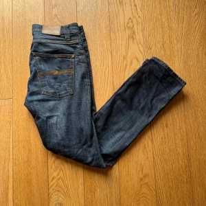 Mörkblå jeans från Nudie Jeans grim trim - Snygga mörkblå jeans från Nudie. Jeansen har en rak passform och är tillverkade i slitstarkt denim med subtila slitningar och Nudie-logga på bakfickan.