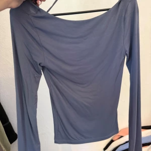 Grå långärmad topp med öppen rygg - Säljer en stilren grå långärmad topp med en snyggt öppen rygg. Toppen har en tight passform och är tillverkad i ett mjukt, stretchigt material som känns skönt mot huden. Perfekt för dig som vill ha en enkel men ändå unik look.