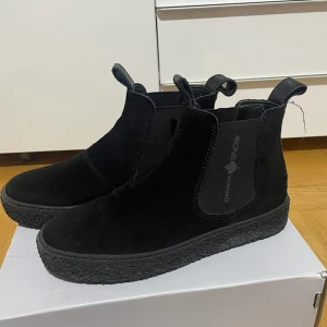 Svarta chelsea boots från Canada Snow - Snygga svarta chelsea boots från Canada Snow i mocka med elastiska paneler på sidorna och dragflikar fram och bak. Skorna har en platt sula och stilren design som passar perfekt till höst och vinter. Perfekta för dig som gillar klassiska och bekväma boots.