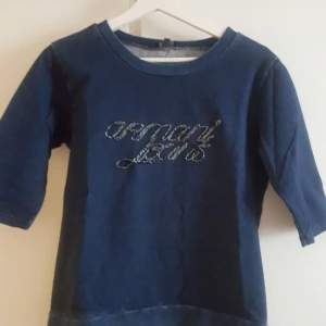 Blå tröja från Armani Jeans M  - Mörkblå tröja från Armani Jeans med glittrig logga framtill. Tröjan har rund halsringning och trekvartsärm. Materialet är mjukt och bekvämt, perfekt för en chill look. Snygg detalj med pärlbroderad text på bröstet.