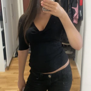 Svart omlottopp med v-ringning - Säljer en svart omlottopp med v-ringning och trekvartsärm. Toppen har en tight passform och är perfekt för dig som gillar en stilren och enkel look. Materialet känns mjukt och följsamt mot kroppen.