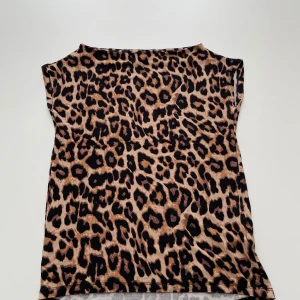Leopardmönstrad topp i beige och svart - Säljer en snygg topp med leopardmönster i beige och svart. Modellen är ärmlös med bred halsringning som kan bäras lite off-shoulder. Tunt och mjukt material. Storlek M men passar S.