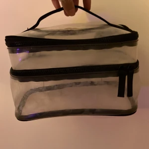 Transparent necessär med svart dragkedja - Praktisk och rymlig transparent necessär med svart dragkedja och handtag. Perfekt för att organisera smink, hudvård eller andra småprylar. Väskan är rektangulär och har två separata fack med dragkedjor för enkel åtkomst.